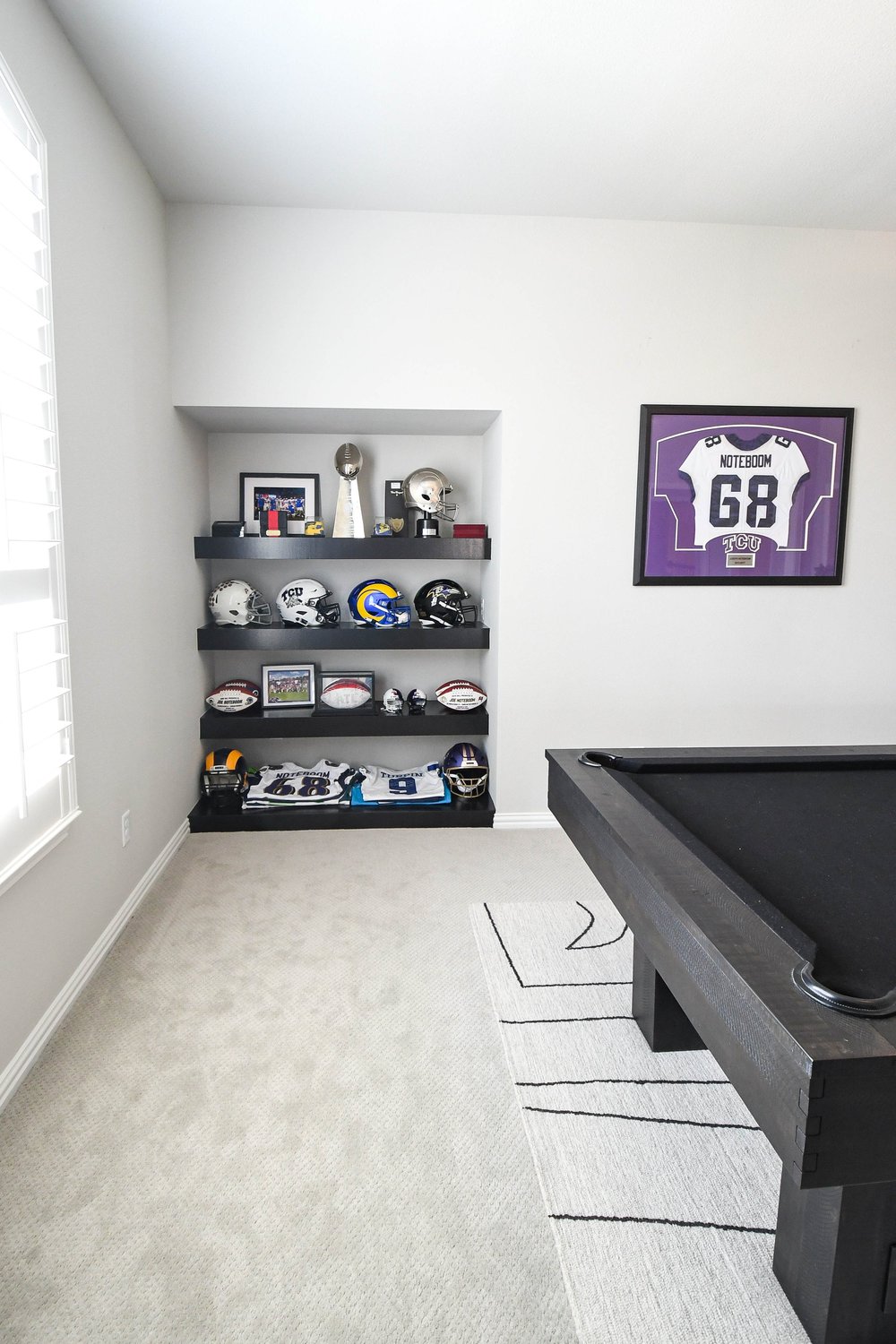Game room with a black pool table and a lit alcove of football memorabilia