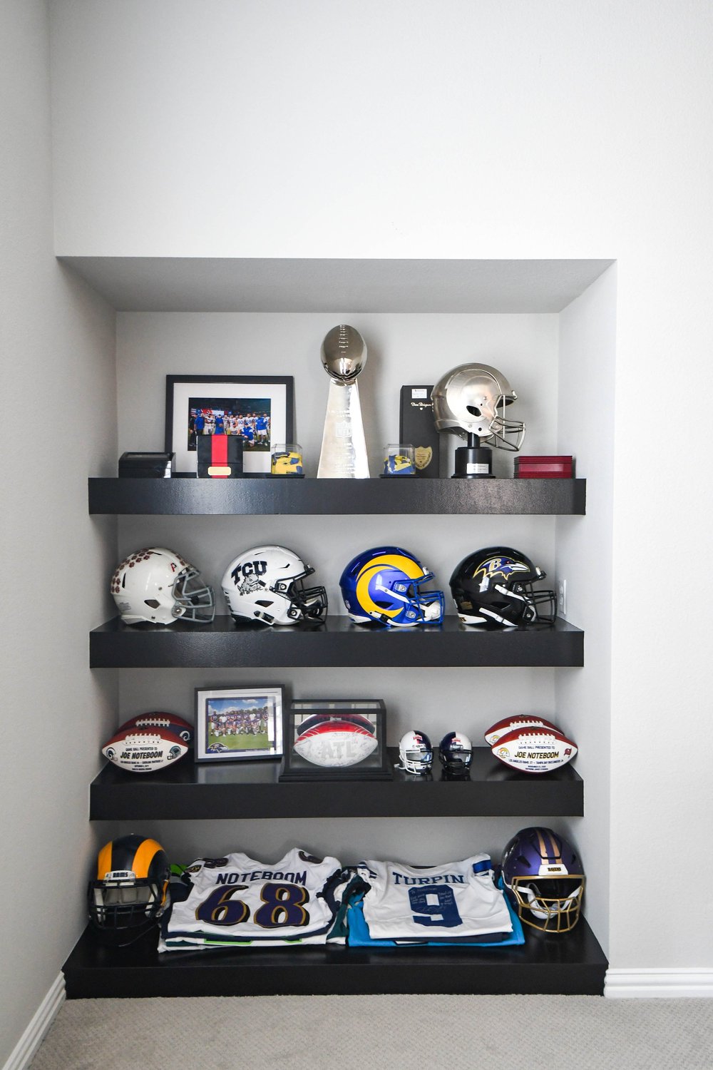 Four floating shelves of collected helmets, footballs and jerseys in the alcove