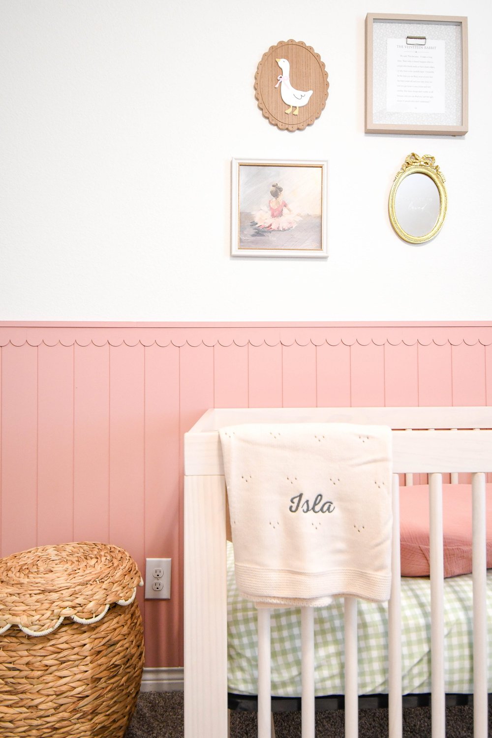 White crib against pink scalloped board and batten with a monogrammed blanket