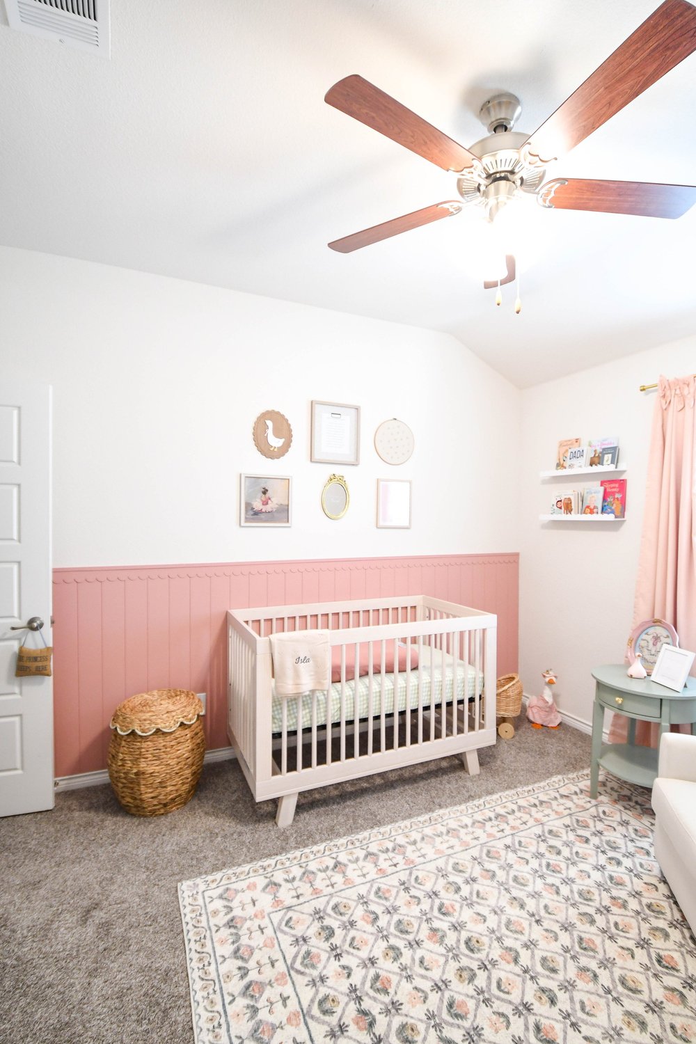Nursery with the crib, gallery wall and a floral rug under a ceiling fan