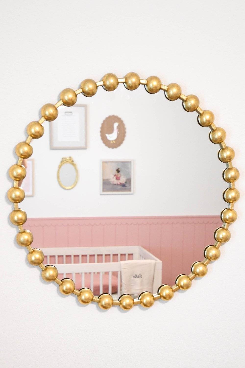 Gold beaded round mirror reflecting the gallery wall and crib