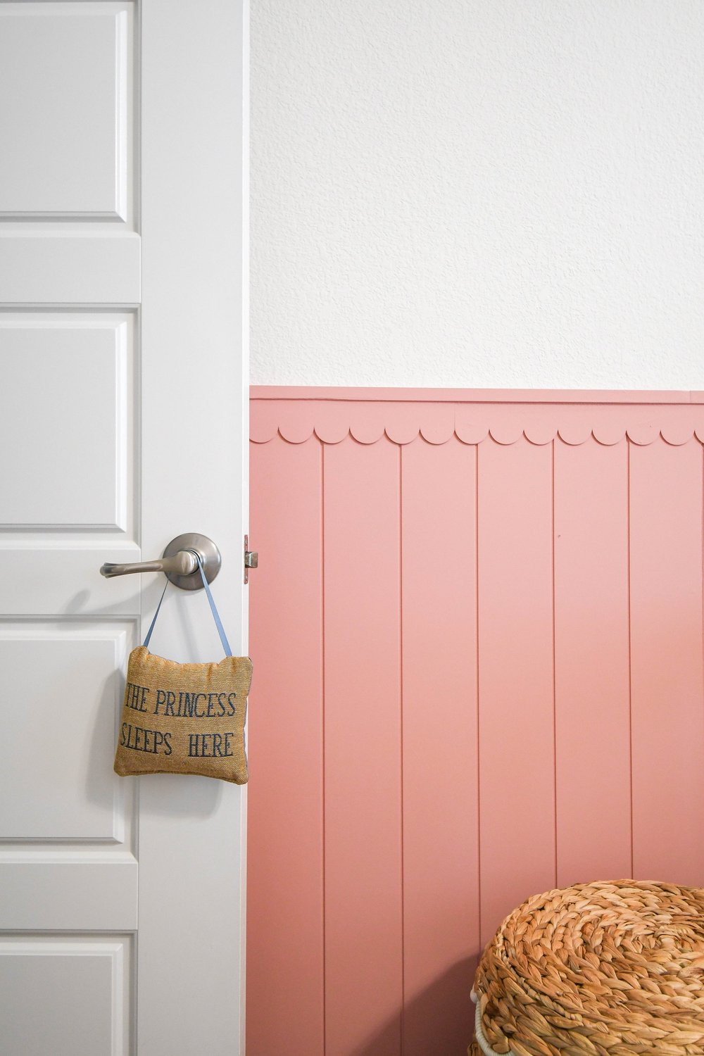 Pink scalloped panelling behind the door with a woven basket on the handle