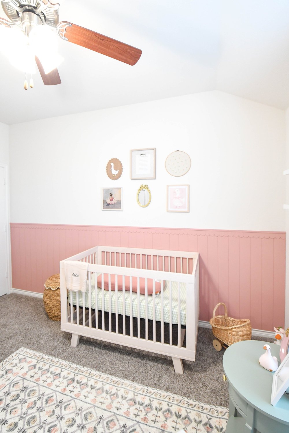 The nursery wall with the crib, floral rug and mint table