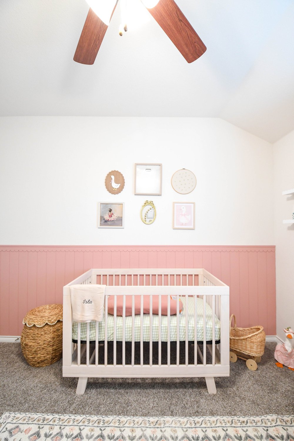 The crib centred on the pink panelled wall below the framed prints