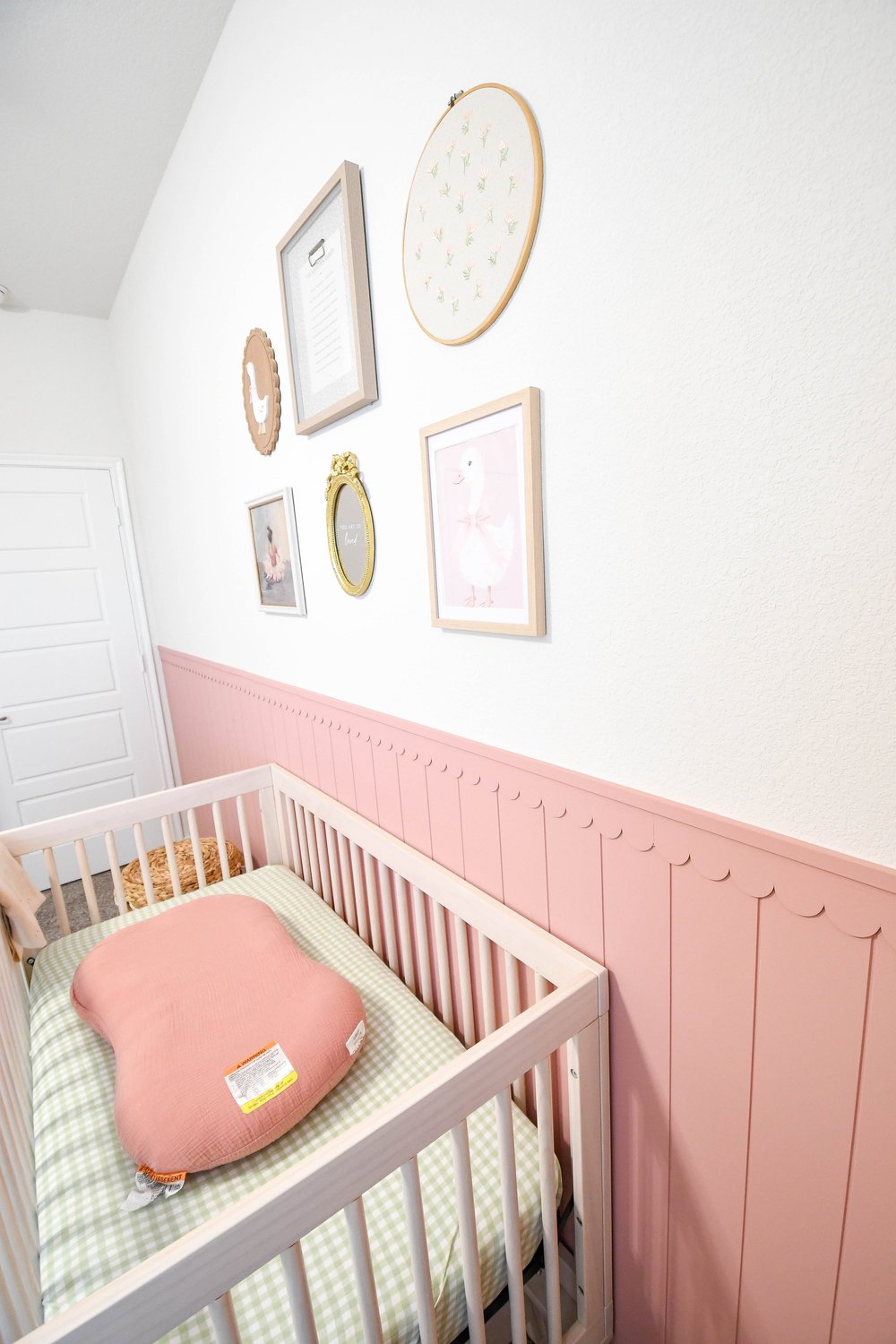 The crib's gingham sheet and pink pillow against the scalloped panelling