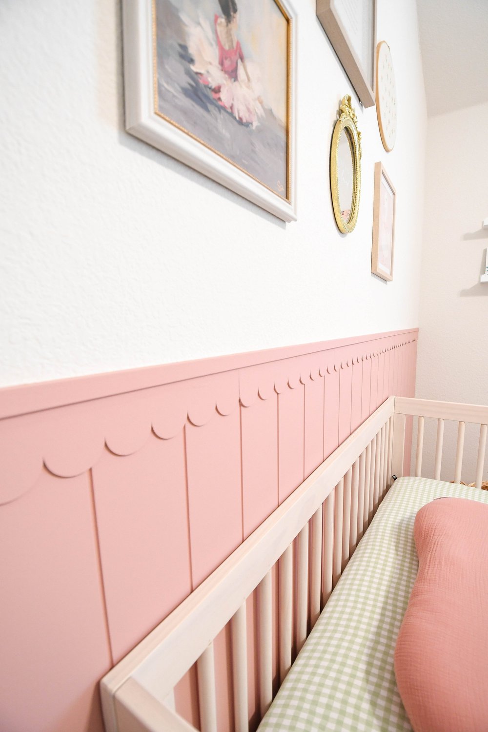 The framed ballet artwork above the scalloped pink panelling and crib