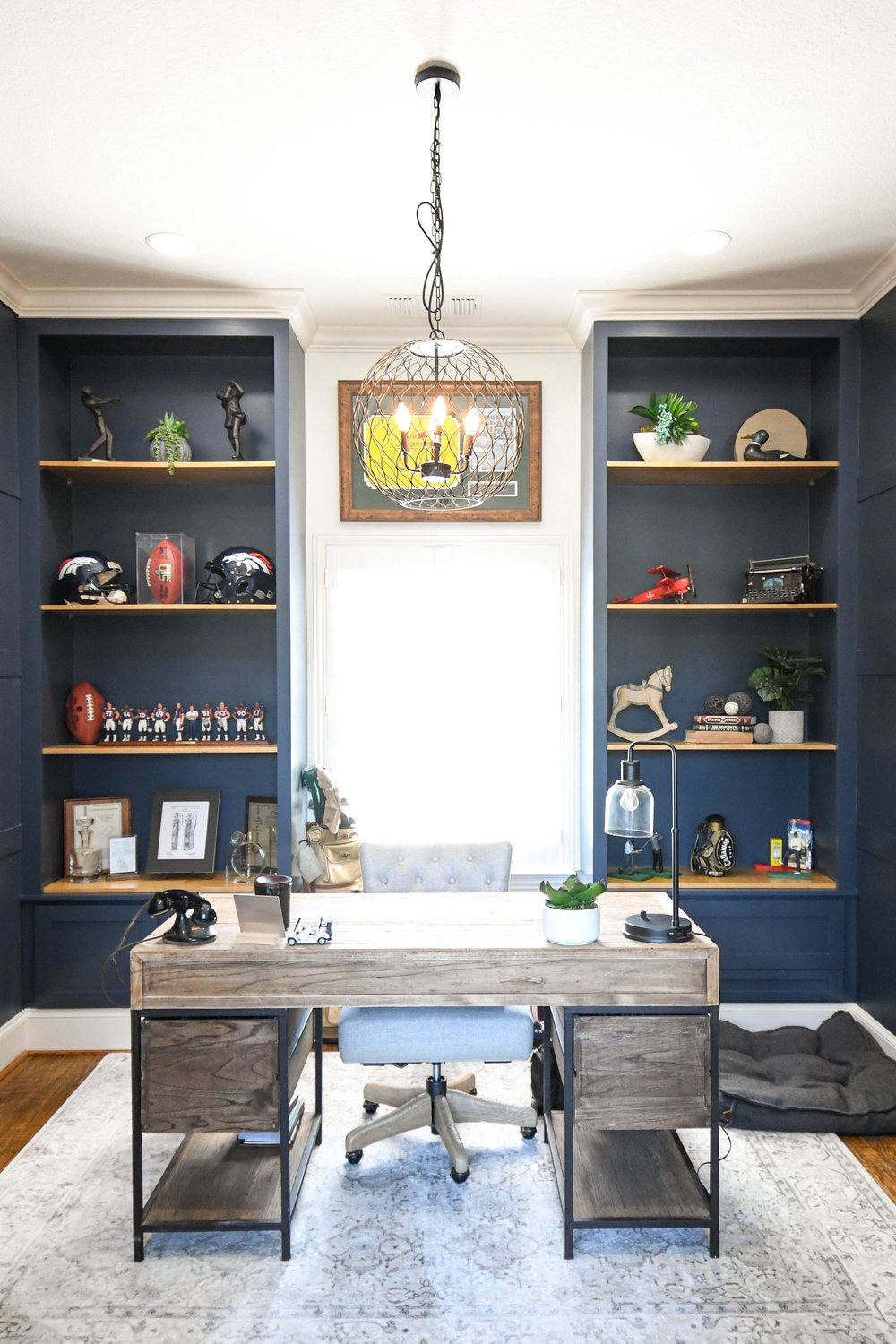 Navy office with a reclaimed wood desk between built-in shelving