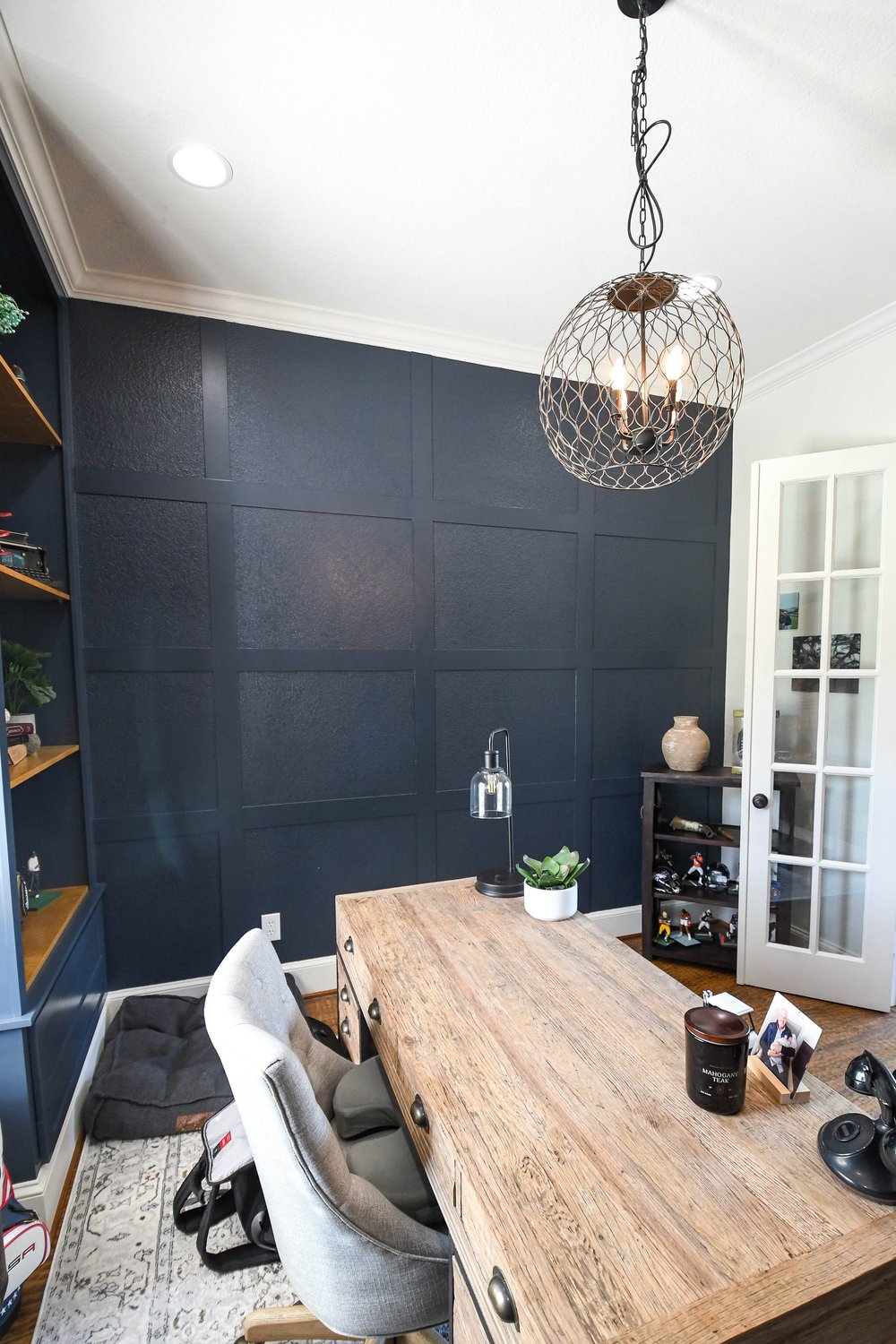 Board and batten navy wall behind the wood desk and cane chair