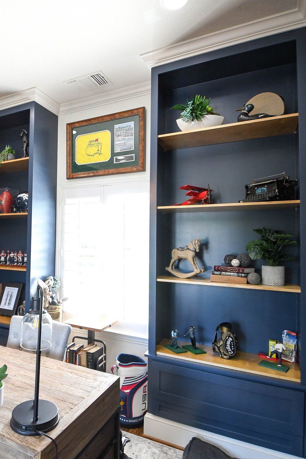 Navy built-ins with oak shelves holding helmets, plants and collectibles