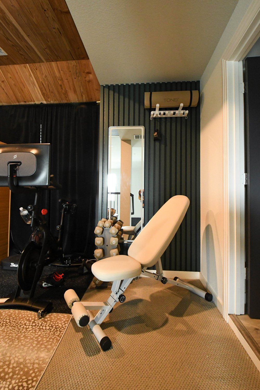 Home gym corner with a bench, exercise bike and mirror against a black fluted wall