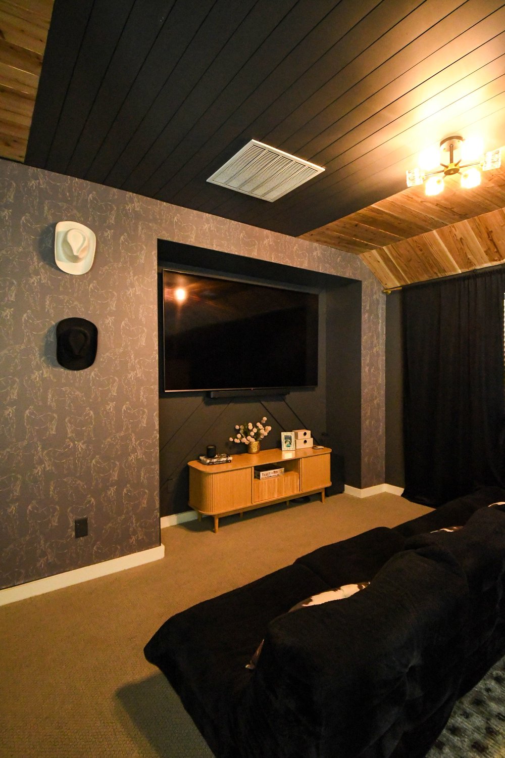 Home theatre with a mounted screen, dark walls and a black sectional