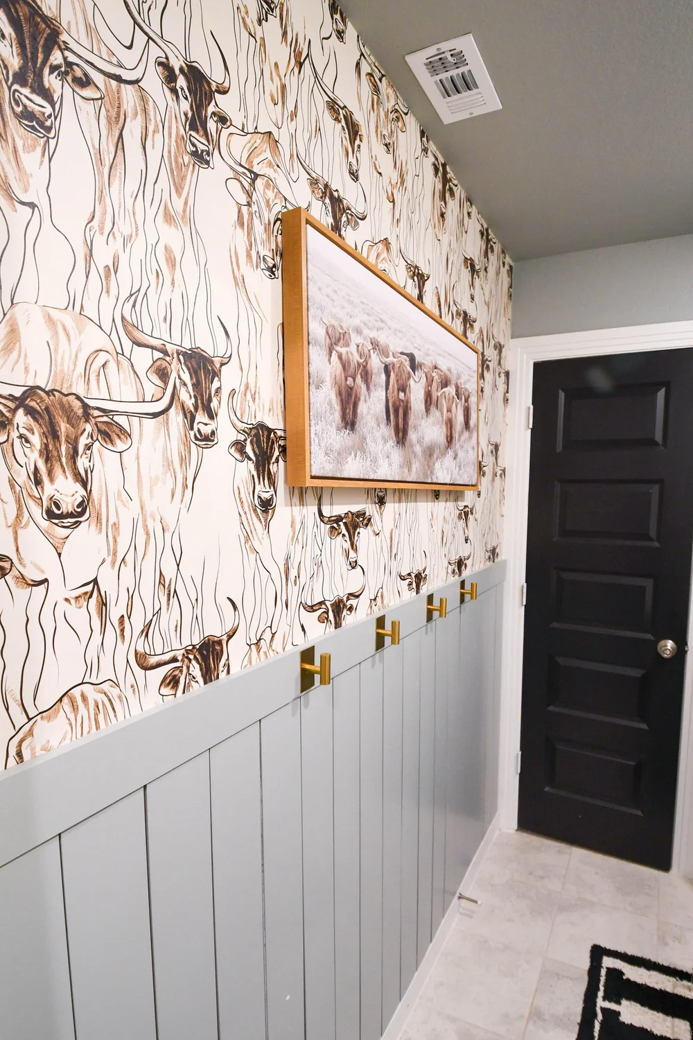 Longhorn wallpaper and sage panelling running down the wall to the dark door