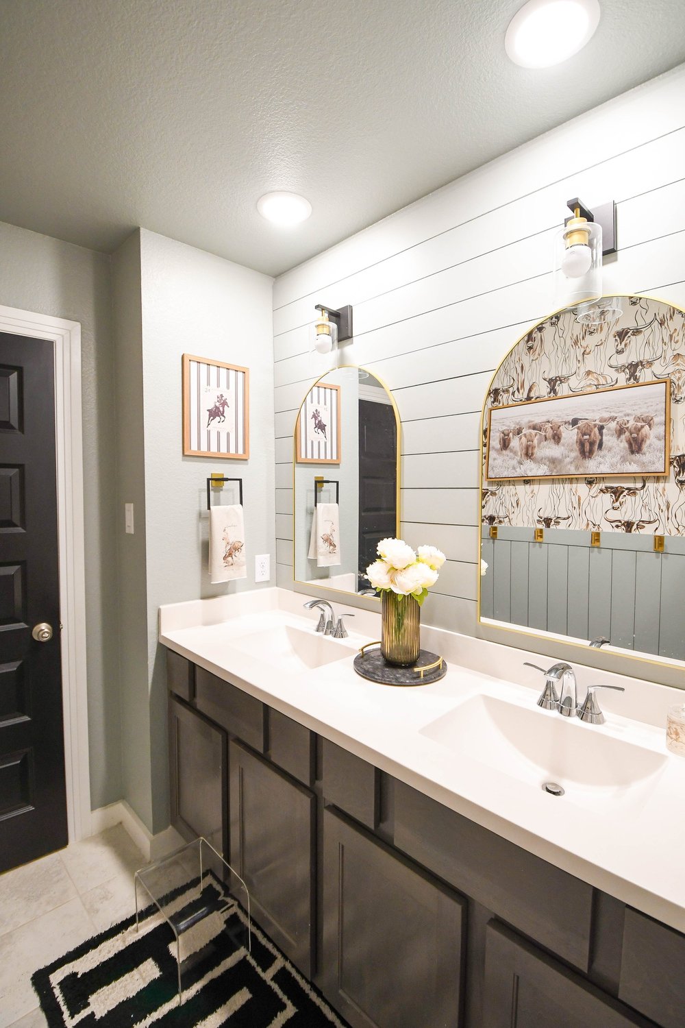 Double vanity with two arched gold mirrors above a black and white runner