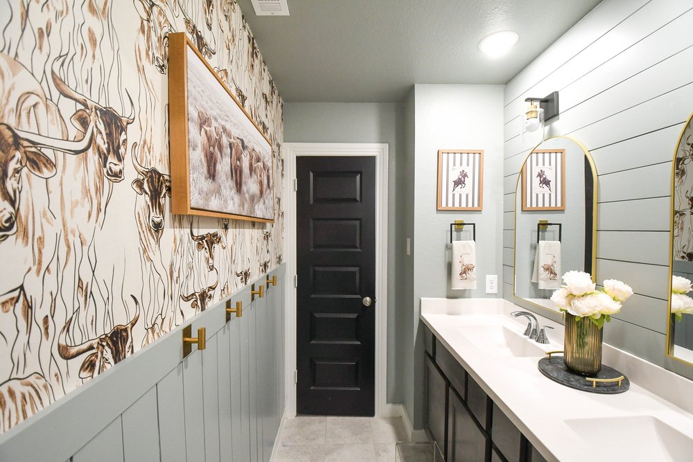 The bathroom lengthwise with the wallpaper, vanity and framed cattle canvas