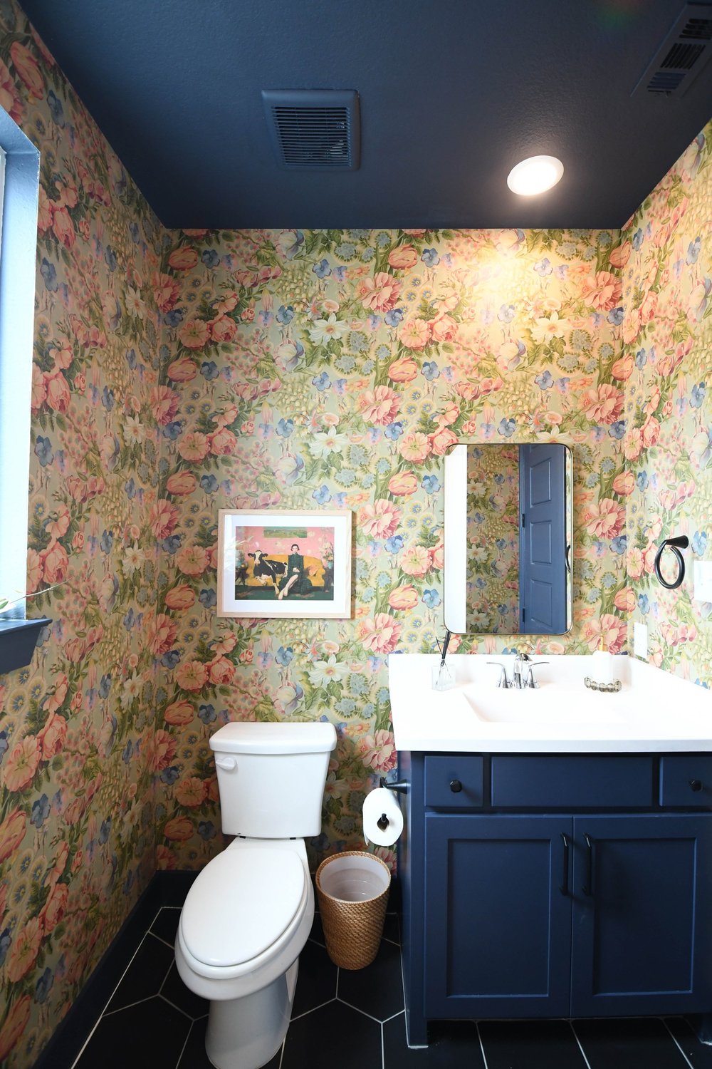 Toilet and navy vanity below the framed print on the black hexagon tile floor