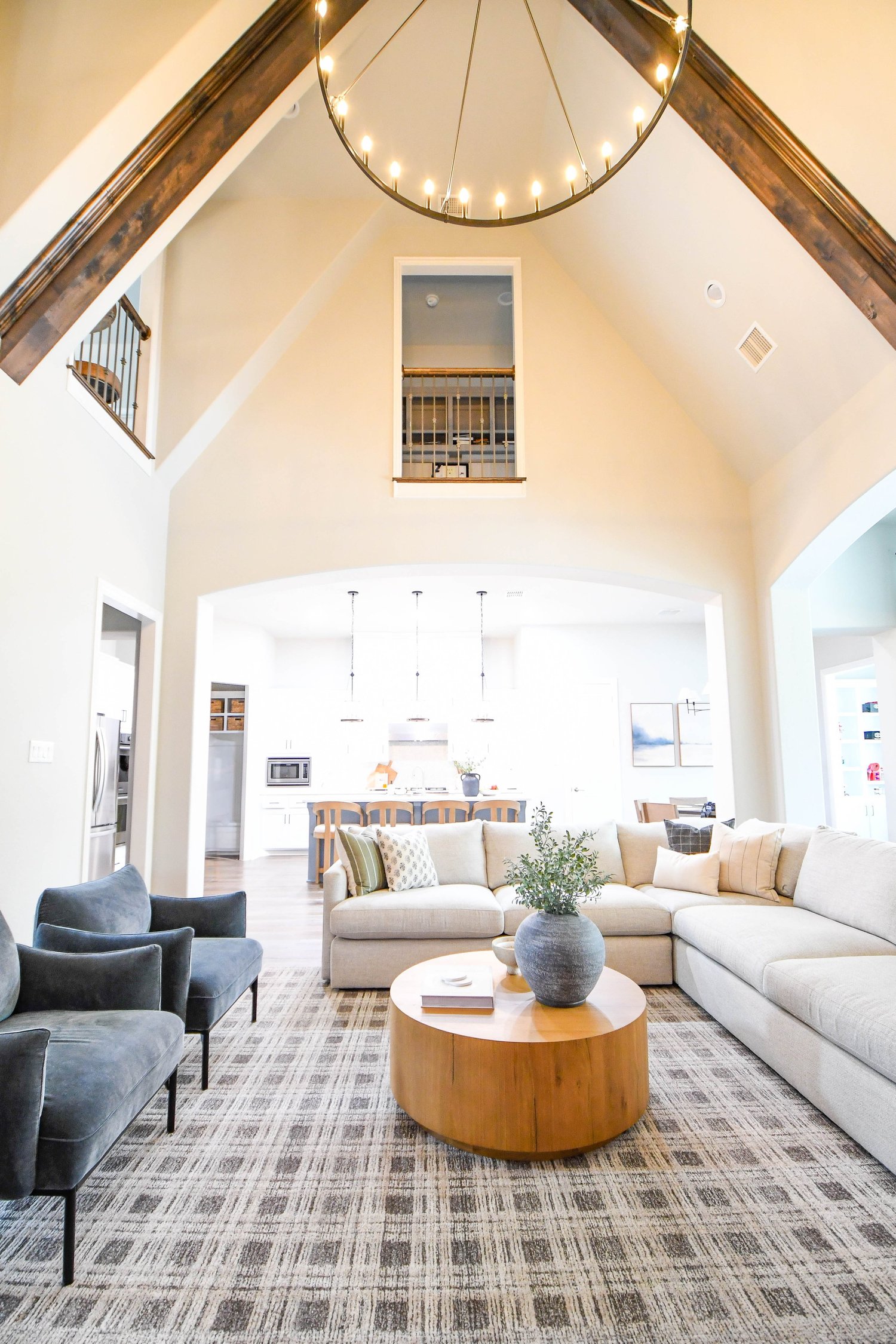 A vaulted great room with exposed beams, a ring chandelier and a sectional sofa
