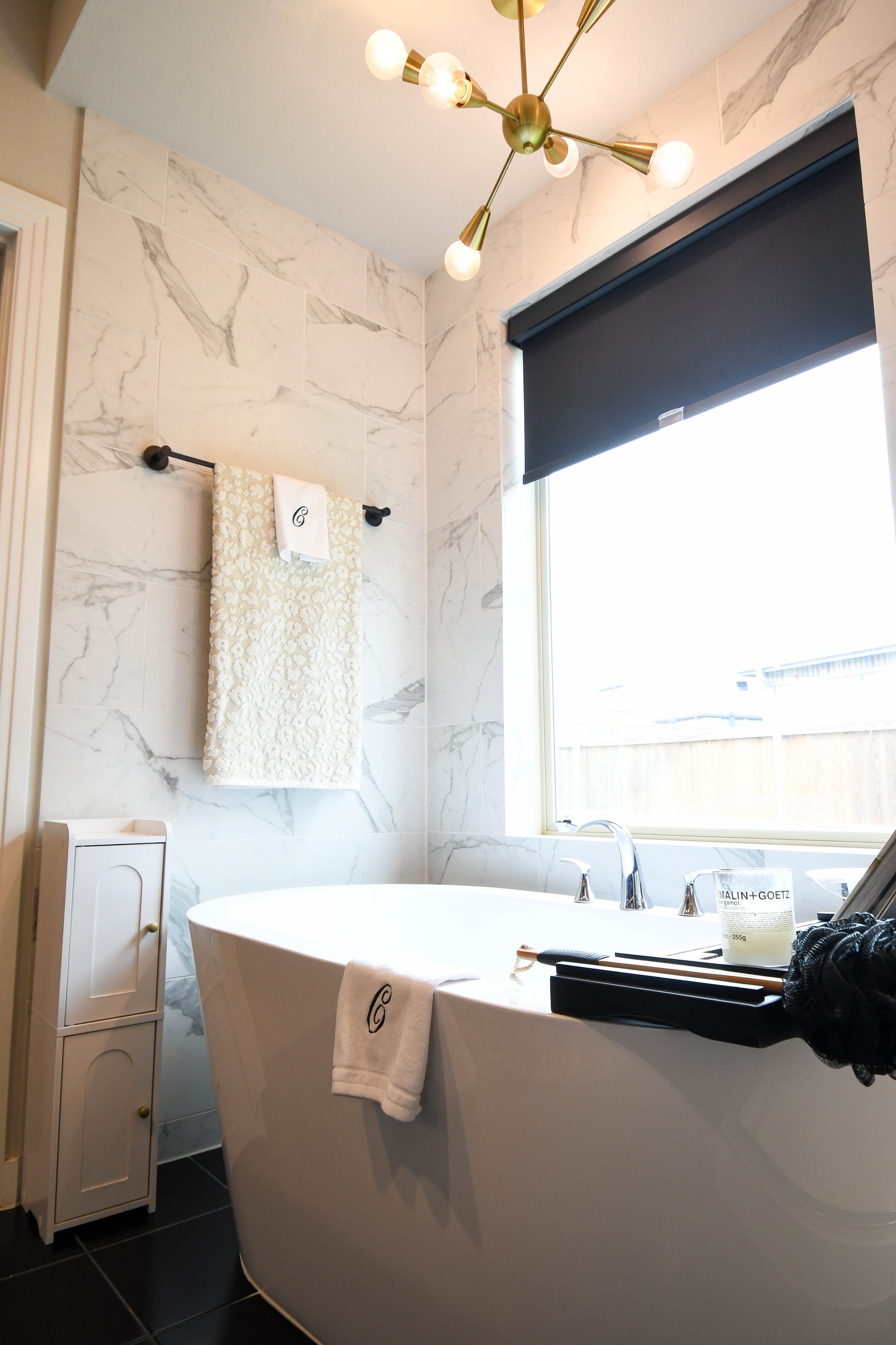 A marble-tiled bathroom with a freestanding tub and a brass chandelier